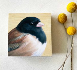 Overhead view of painting of a dark eyed junco on wood by Maggie Hurley